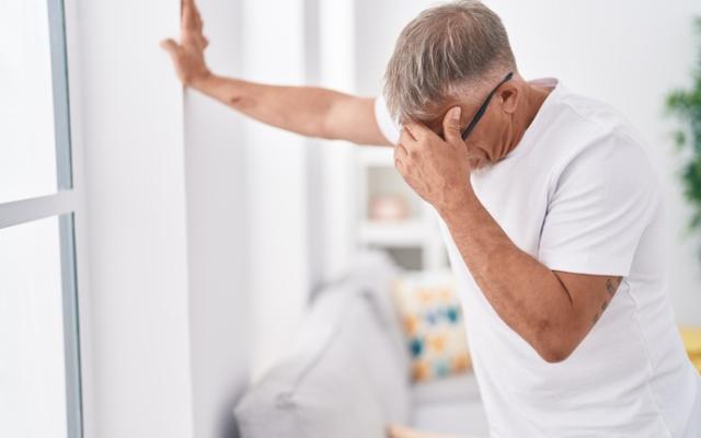 Hombre con mareo al levantarse apoyado en la pared de su casa